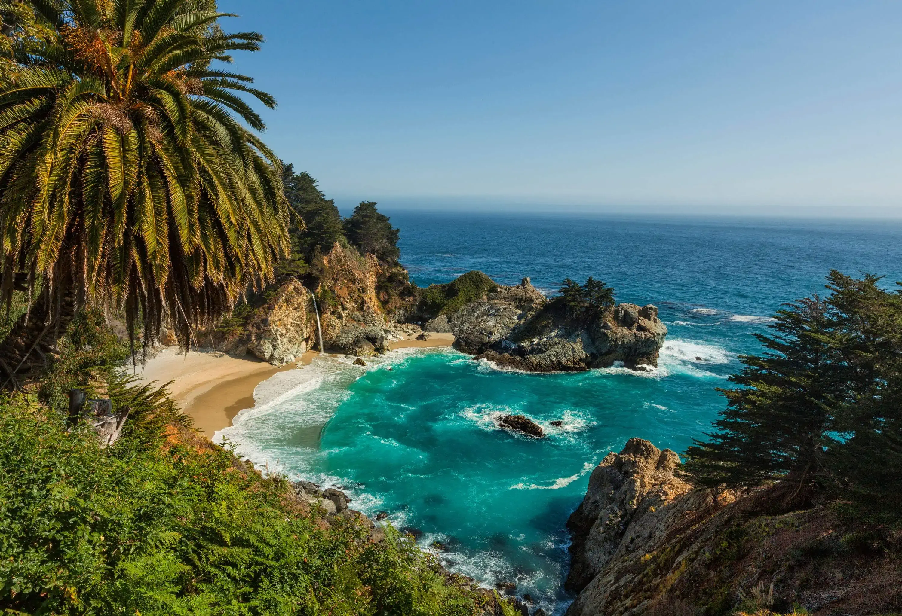 A picturesque paradise of a rocky forested island with a sandy shore surrounded by the turquoise sea.