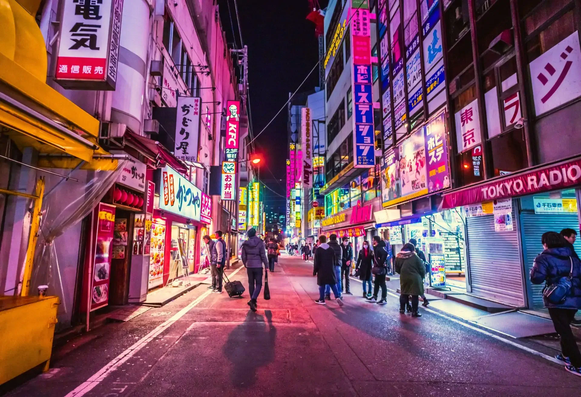 A view of a street in Tokyo with a few people, colorful signs and neon lights.